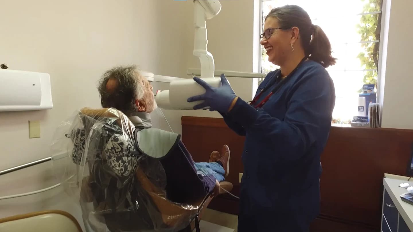 A hygienist positioning the X-ray arm for a patient in the chair