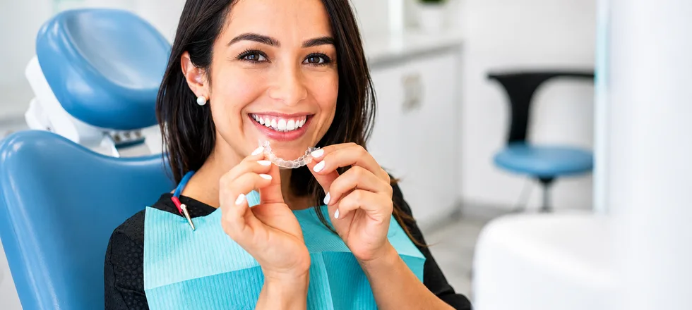 A smiling patient holding her clear aligner tray at her consultation
